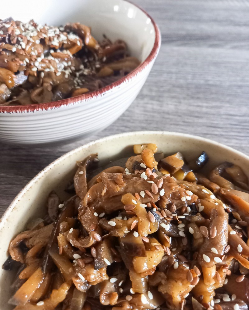 Two bowls of carob pasta, mushrooms and eggplant, sprinkled with sesame seeds.