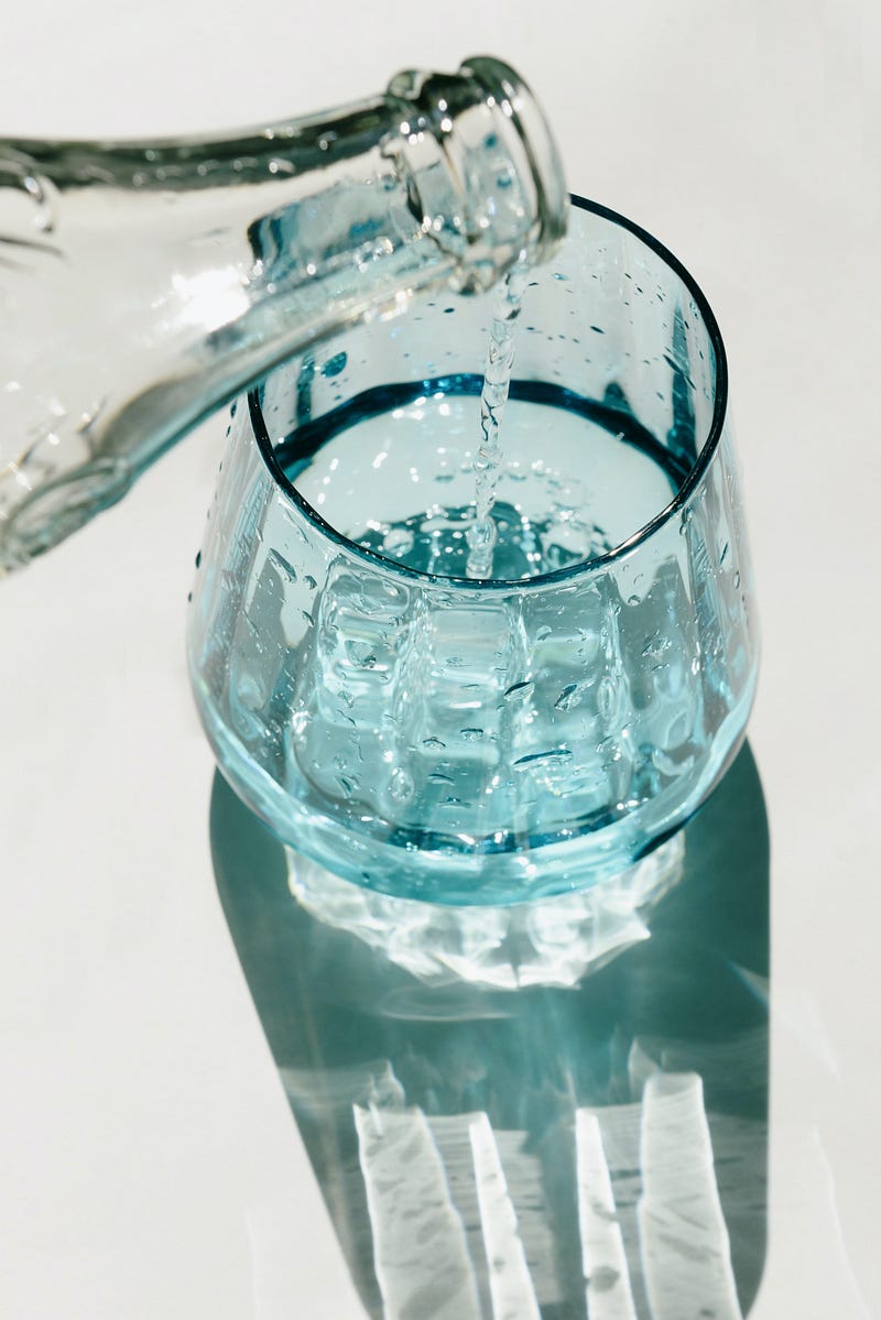 Water is pouring from a glass bottle into a glass, sitting on a white surface.