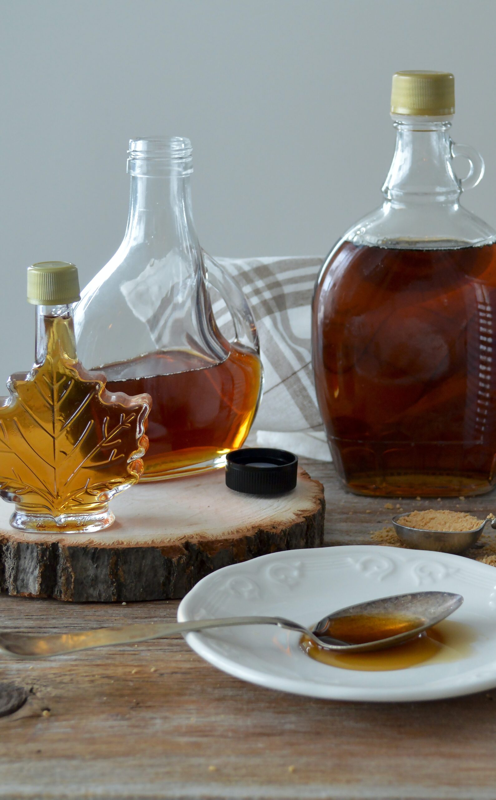 A display of 3 glass bottles with maple syrup, a plate, and a spoon full of maple syrup